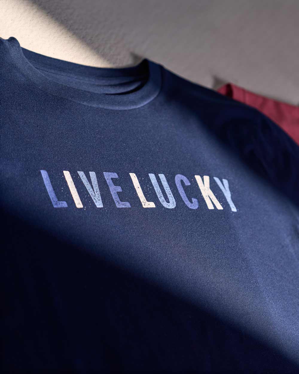 A blue, red, and green t-shirt featuring the text "Live Lucky" on a grey background.