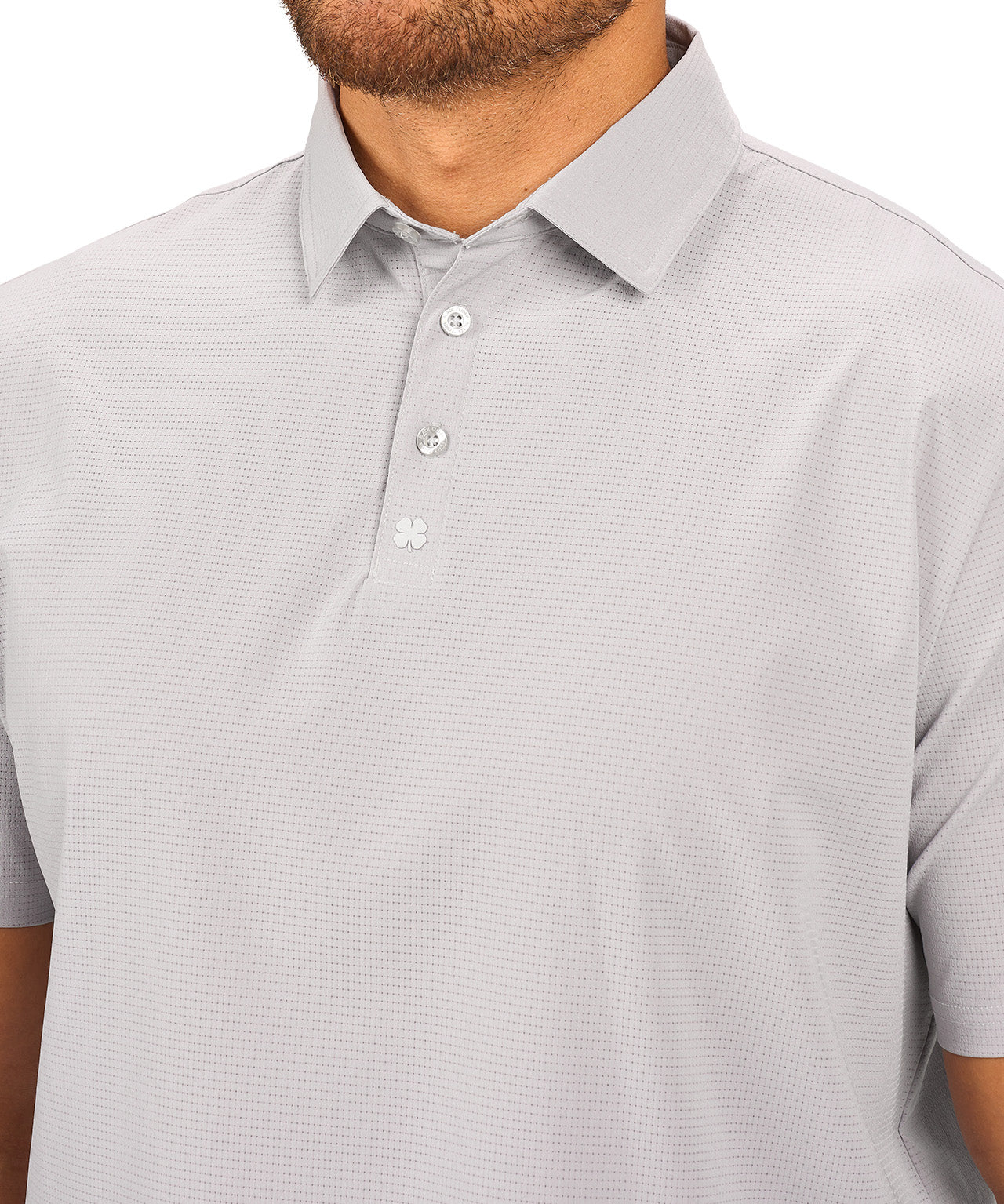 Man wearing light grey polo from Black Clover with a small clover near the buttons