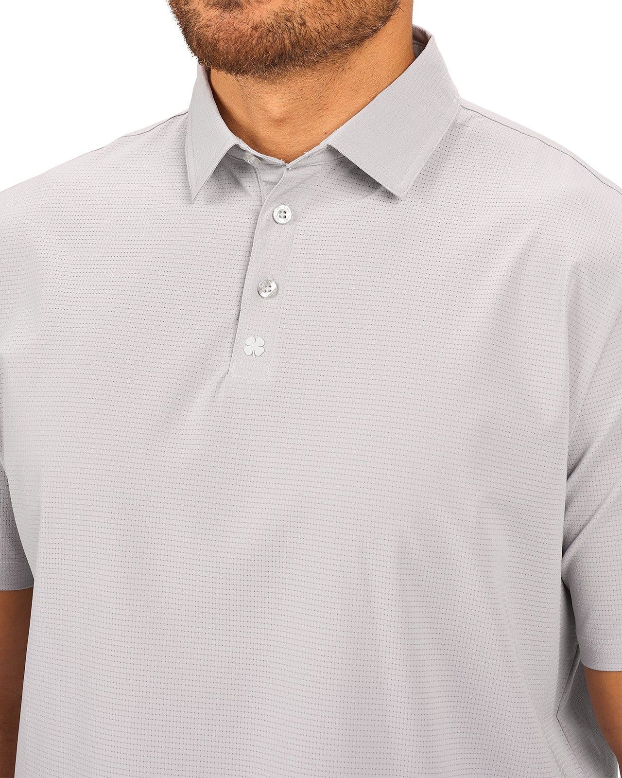 Man wearing light grey polo from Black Clover with a small clover near the buttons