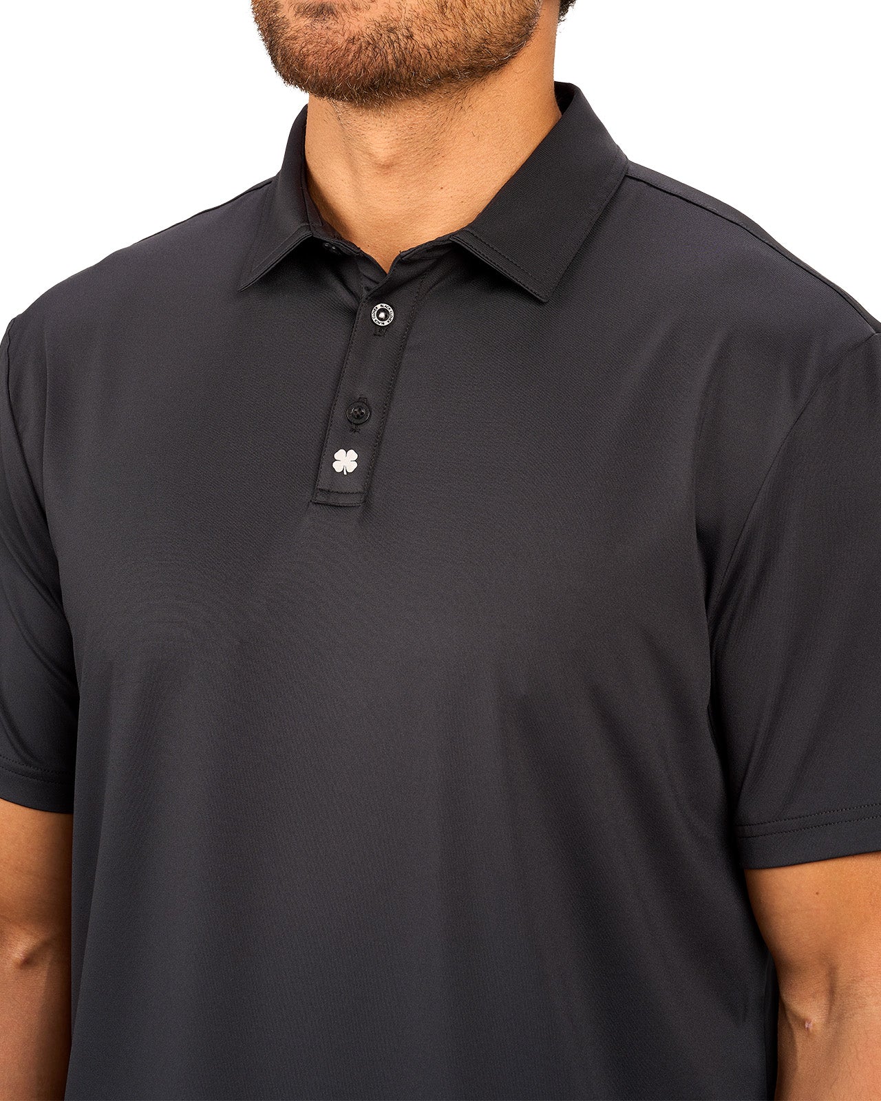 Man wearing black polo from black clover featuring a small clover logo below the bottom button