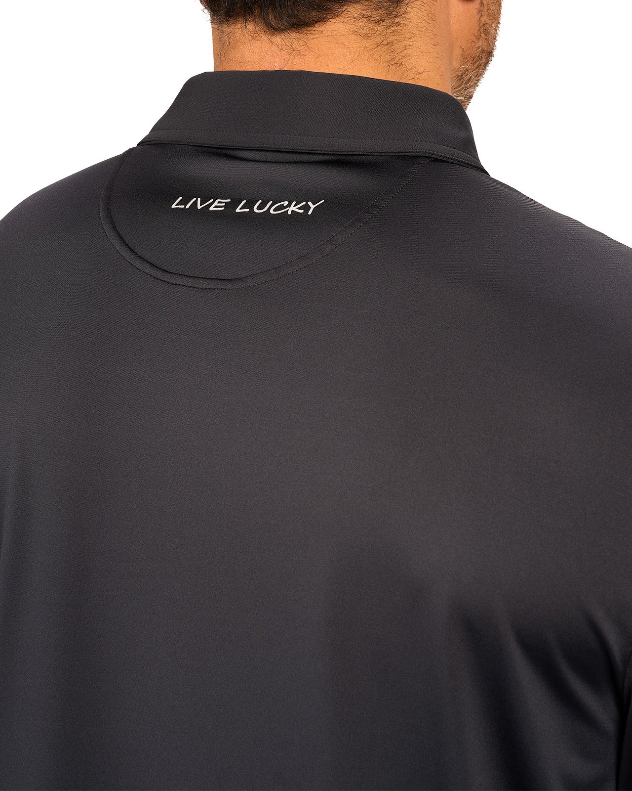 Man wearing black polo from black clover featuring a small clover logo below the bottom button