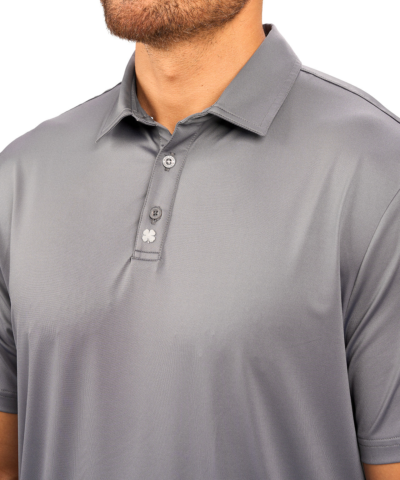 Man wearing charcoal grey polo from black clover featuring a small clover logo below the bottom button