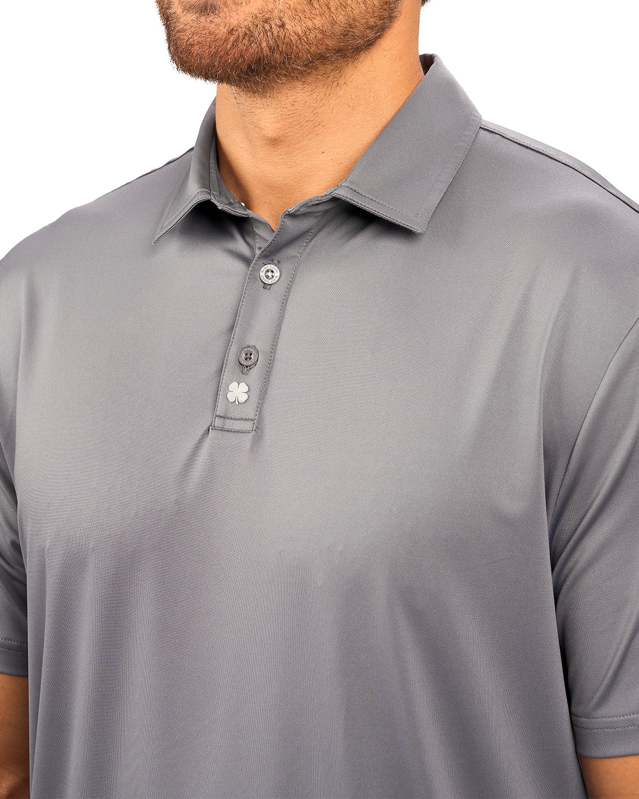 Man wearing charcoal grey polo from black clover featuring a small clover logo below the bottom button