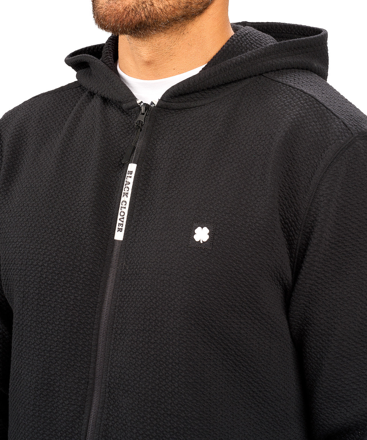 Man wearing black zip up hoodie from Black Clover featuring small clover icon on the left chest