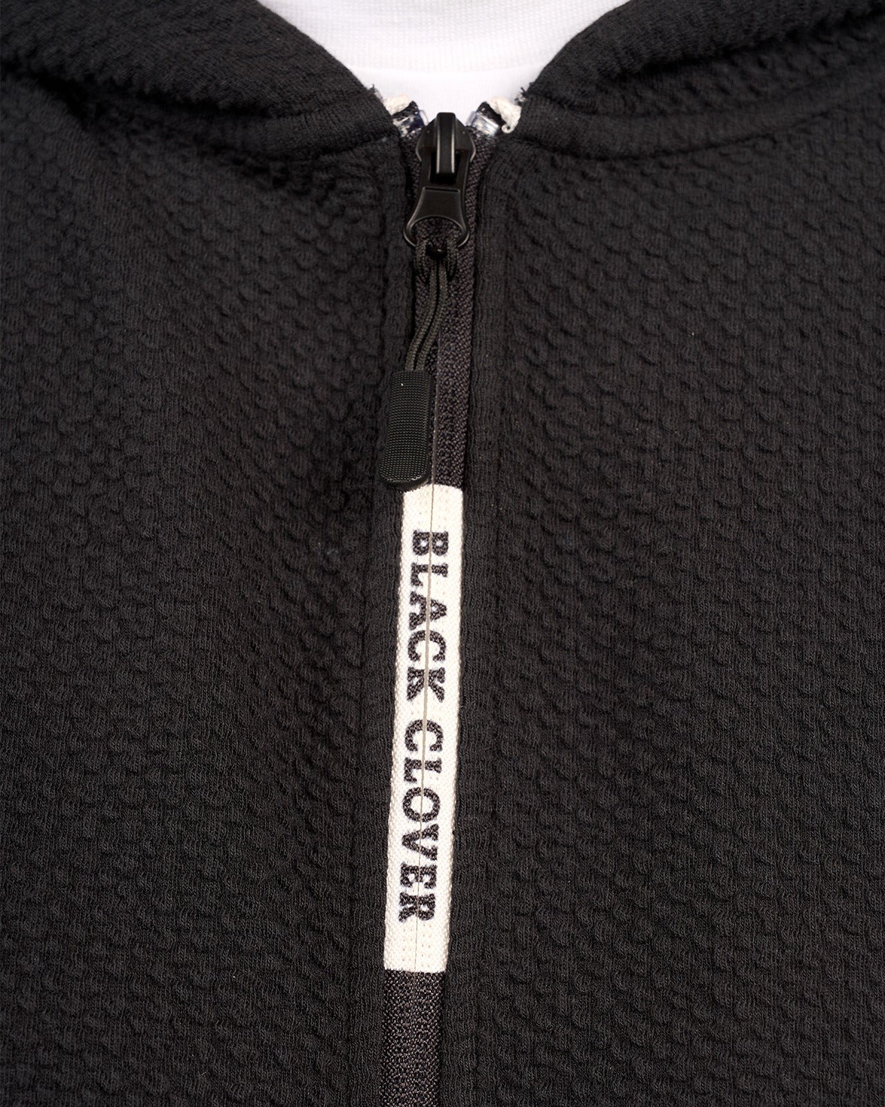 Man wearing black zip up hoodie from Black Clover featuring small clover icon on the left chest