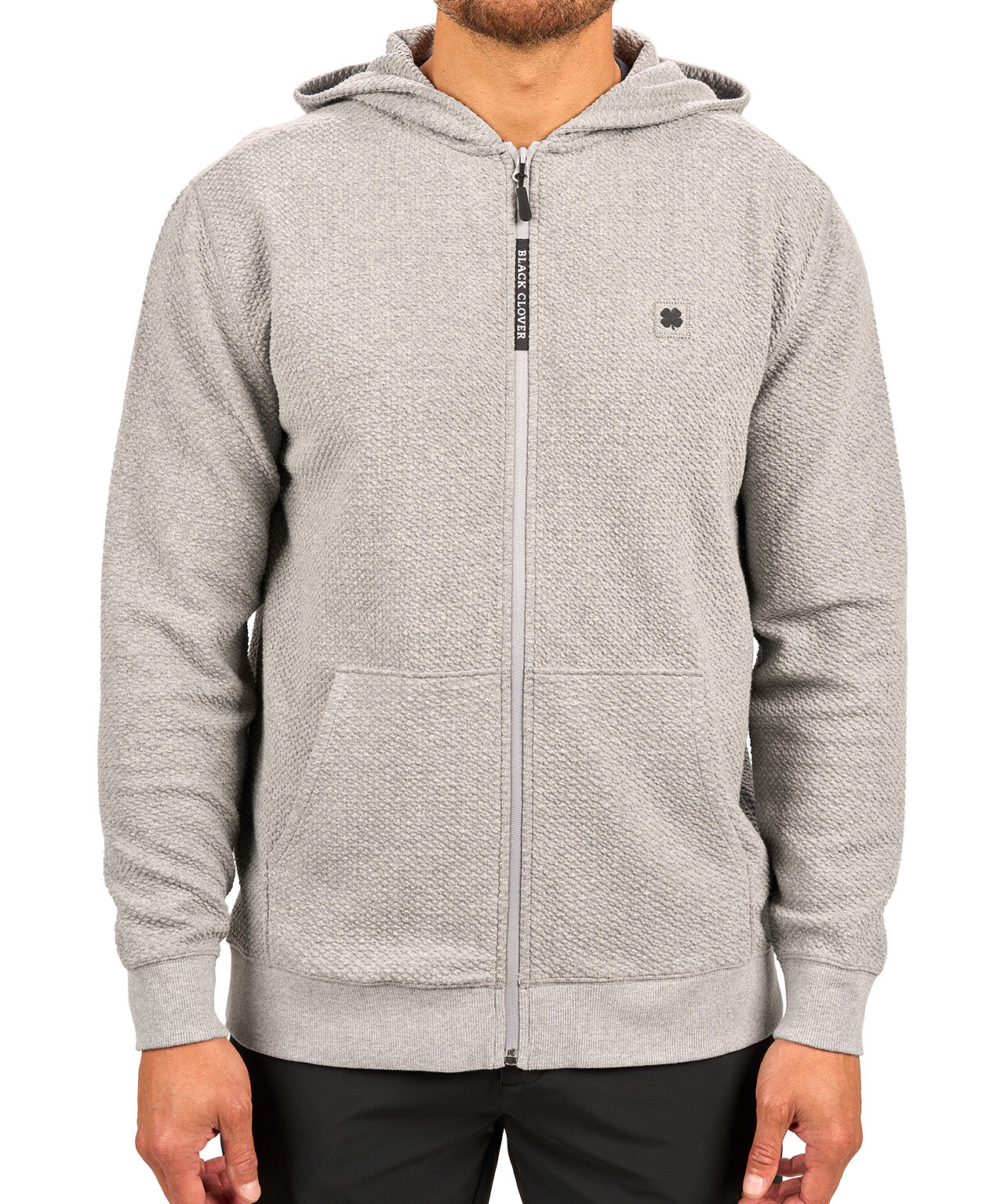 Man wearing oatmeal colored zip up hoodie from Black Clover featuring small clover icon on the left chest