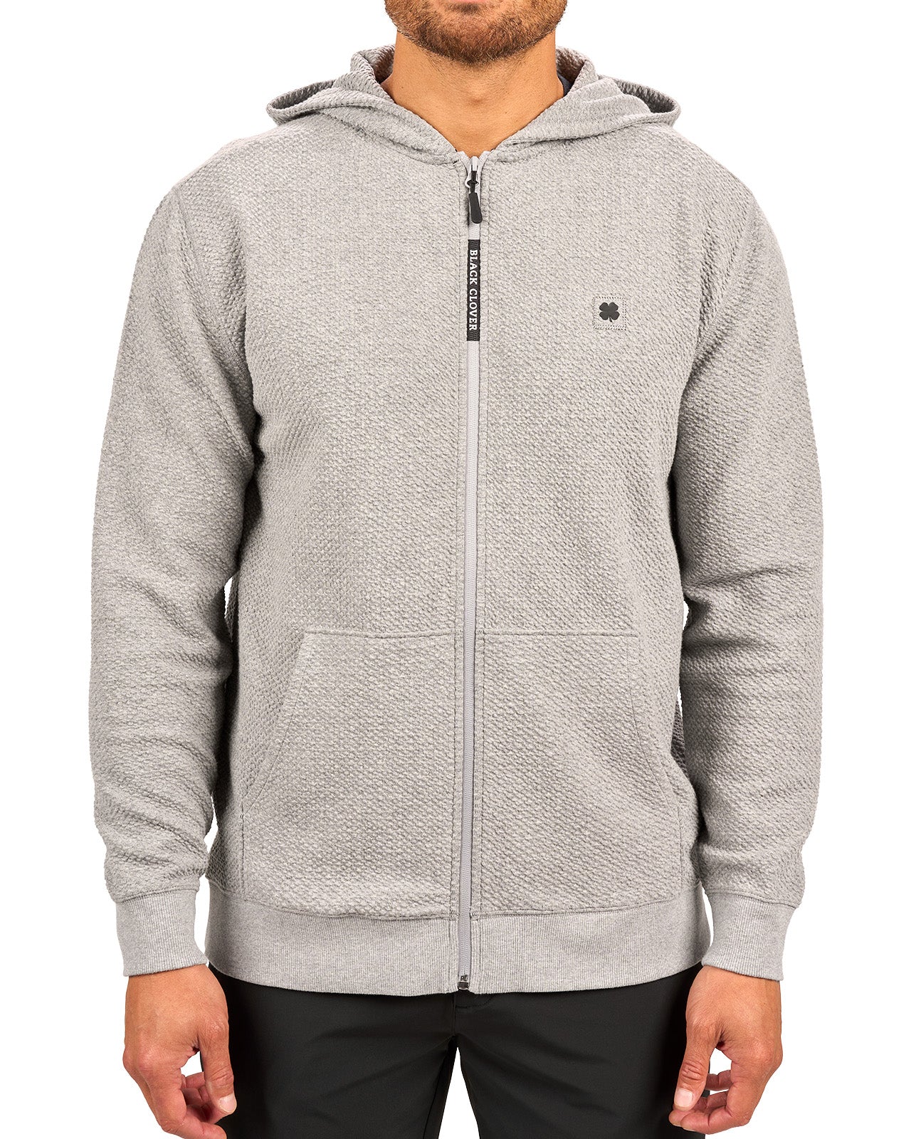 Man wearing oatmeal colored zip up hoodie from Black Clover featuring small clover icon on the left chest