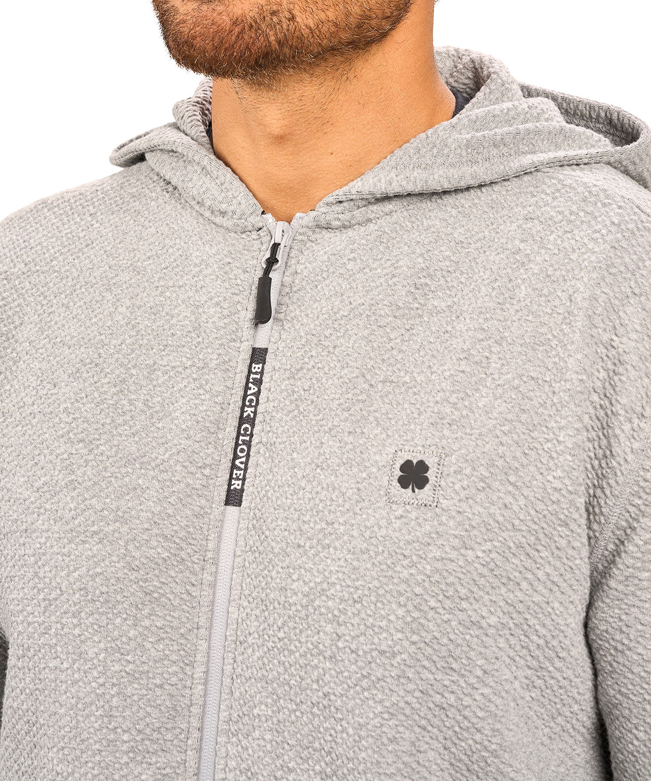 Man wearing oatmeal colored zip up hoodie from Black Clover featuring small clover icon on the left chest