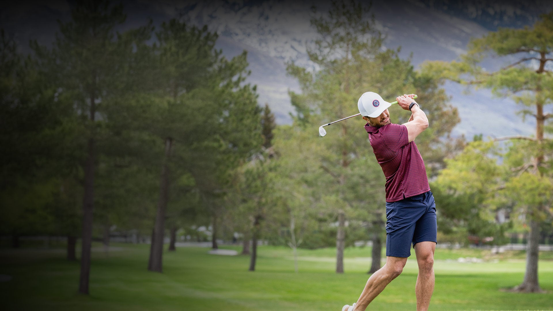 Golfer in action on a golf course with trees and mountains in the background